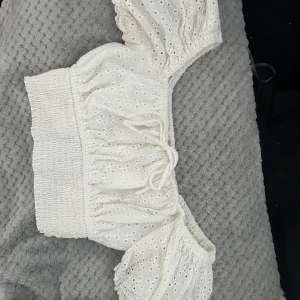 Vit croppad blus från FB Sister - Superfin vit croppad blus från FB Sister med broderade hål och puffärmar. Smockad midja och knyt framtill ger en söt och trendig look. Perfekt till sommaren!