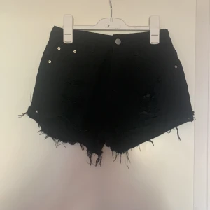 Svarta jeansshorts med fransar från SHEIN - Svarta jeansshorts från SHEIN i modellen Petite XS. Shortsen har fransiga benslut och slitna detaljer framtill för en edgy look. Klassisk femficksmodell med knapp och dragkedja. Perfekta för sommaren!