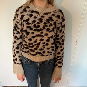 Beige leopardmönstrad stickad tröja - Säljer en beige stickad tröja med leopardmönster i svart och brunt. Tröjan har långa ärmar, rund halsringning och ribbade muddar vid ärmslut och nederkant. Perfekt för dig som vill ha en trendig och mysig look.