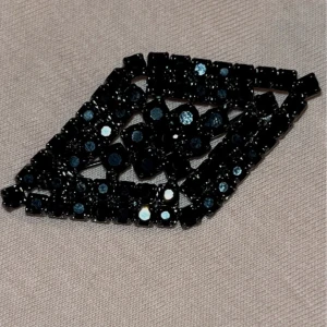 Svart glittrigt brosch i diamantform - Säljer en snygg brosch i diamantform med svarta glittriga stenar. Perfekt accessoar för att lyfta din outfit med lite extra bling. Broschen har ett geometriskt mönster och passar till många olika stilar.