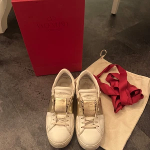 Vita Valentino Garavani sneakers med gulddetaljer - Super trendiga Valentines! Använda men i super bra skick, inga defekter förutom att insidan av skon är lite smutsig då jag använt sula i dem men de borde gå att tvättas bort. Jag är öppen för pris förslag!
