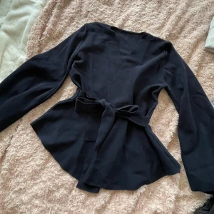 Marinblå  omlottkofta med knytband - Säljer en marinblå omlottkofta med knytband i midjan. Tröjan har lång ärm och är tillverkad i ett mjukt, stickat material. Perfekt för lager-på-lager och enkel att styla till olika outfits.