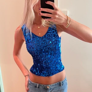Blå paljettopp - Säljer en glittrig blå paljettopp med ärmlös design och rundad halsringning. Toppen är figurnära och perfekt för att sticka ut. Materialet är täckt av blå paljetter som ger en snygg glansig effekt.