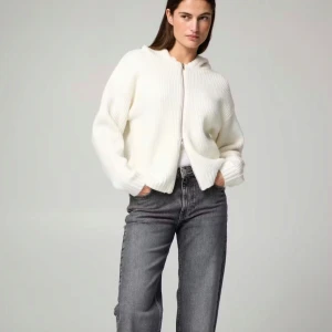 Vit stickad hoodie med dragkedja - Säljer en vit stickad hoodie med dragkedja framtill. Jackan har en avslappnad passform, huva och ribbad struktur. Perfekt för lager-på-lager och enkel att matcha med jeans eller kjol.