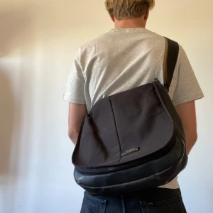 Svart messenger bag från Samsonite - Säljer en svart Messenger bag från Samsonite med justerbar axelrem och praktiskt lock. Väskan har flera fack, bland annat ett med dragkedja och meshficka på insidan. Perfekt för att bära med sig det viktigaste till skolan eller stan. Det man drar i i blixtlåsen har ramlat av men funkar finfint ändå.