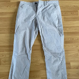Gråa chinos från Tommy Hilfiger - Snygga gråa chinos från Tommy Hilfiger i klassisk rak modell. Byxorna har normal passform, bälteshällor och stängs med knapp och dragkedja. Perfekta för en stilren och avslappnad look. 30/30