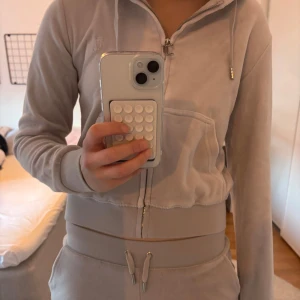 Ljusgrått set från Juicy Couture - Säljer ett ljusgrått set med hoodie och shorts från Juicy Couture. Tröjan har fickor på magen och ribbade muddar vid ärmslut och nederkant. Setet säljs pågrund av att det inte kommer till användning och är som nytt! 
