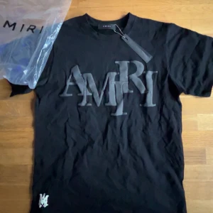 Svart t-shirt från Amiri med stor logga - Säljer en svart t-shirt från Amiri med stor, upphöjd logga framtill. Klassisk rund halsringning och korta ärmar. Perfekt för dig som gillar streetwear och vill ha något stilrent men ändå iögonfallande.