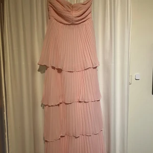 Ljusrosa axelbandslös långklänning från Lulus - Säljer en romantisk ljusrosa långklänning från Lulus. Klänningen är axelbandslös med fina volanger i flera lager och har dragkedja i ryggen. Perfekt för bal. Den passade mig i längden och jag är 175cm lång. Endast använd en gång