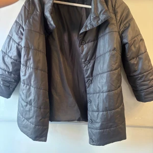 Grå trekvartsärmad jacka med knappar - Jackan går att göra till trekvartsärmad, men även hel ärmar. Säljer en grå pufferjacka med knäppning framtill och hög krage. Jackan har långa ärmar och är quiltad för extra värme. Perfekt för kyliga dagar och enkel att matcha med olika outfits. Storlek s/m