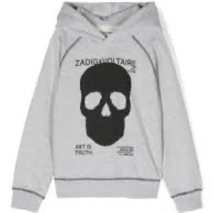 Grå hoodie med döskalle från Zadig & Voltaire - Säljer en grå hoodie från Zadig & Voltaire med stor svart döskalle på bröstet och textdetaljer. Tröjan har huva och långa ärmar, perfekt för en cool och avslappnad stil.