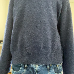 Mörkblå stickad tröja - Mysig mörkblå stickad tröja med rund halsringning och långa ärmar. Tröjan har en klassisk, enkel design med ribbade muddar vid ärmslut och nederkant. Perfekt för kyligare dagar.