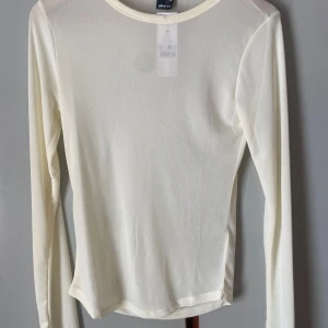 Vit meshtröja från Gina Tricot - Säljer en tunn och transparent vit långärmad topp från Gina Tricot. Perfekt att styla lager på lager eller bära som den är. Enkel och stilren design med rund halsringning. Helt oanvänd med lapp kvar