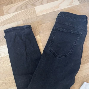 Svarta jeansbyxor från Lee - Säljer ett par svarta jeans från Lee, modell Blake. Klassisk femficksdesign med dragkedja och knapp framtill. Jeansen har en rak passform och är tillverkade i ett mjukt bomullsmaterial. Perfekta för dig som gillar stilrena och tidlösa byxor.