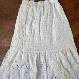 Vit broderad kjol från Lindex - Söt vit kjol från Lindex med broderade hålmönster och resår i midjan. Kjolen har volang nertill och är perfekt för en somrig look. Passar barn i storlek 146/152 (10-12 år). Aldrig använd med prislapp kvar