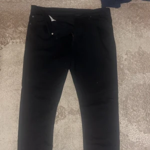 Svarta jeansbyxor från Levi's - Säljer ett par svarta jeansbyxor från Levi's med klassisk femficksdesign och rakt snitt. Byxorna har en liten röd Levi's-tag på bakfickan och stängs med dragkedja och knapp. Perfekta till många olika outfits.