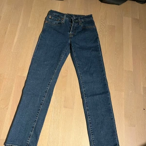 Levi's 501 blå jeans - Klassiska blå Levi's 501 jeans med raka ben och femficksmodell. Byxorna har normal passform, knappgylf och tydliga kontrastsömmar. Perfekta för dig som gillar tidlös denimstil.