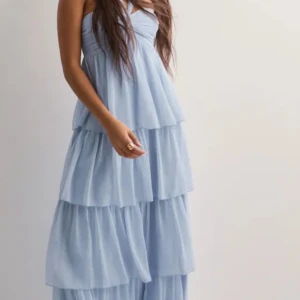 Ljusblå lång klänning från nelly  - Supersöt ljusblå långklänning med halterneck och flera lager volanger Materialet känns lätt och luftigt.köpte denna men har aldrig kommit till användning har kvar lappen. Väldigt fin men passar inte mej men passar nog fint till bal.