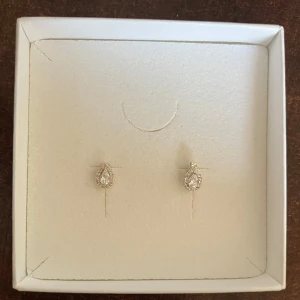 Droppformade örhängen i silver med stenar - Säljer ett par eleganta droppformade örhängen i silverfärg med gnistrande stenar. Perfekta för att ge en extra touch till din look. (Ask ingår inte)
