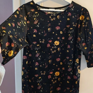 Svart och blommig från Jacqueline de Yong! - Säljer en svart topp med blommigt mönster i gult, lila och rosa från Jacqueline de Yong. Toppen har trekvartsärm och rund halsringning. Jättefin på! Speciellt tsm med beige eller svarta byxor.