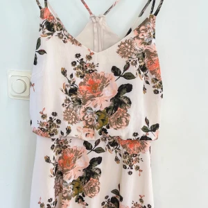 Blommig klänning med smala axelband från Vila - Superfin blommig klänning från Vila med smala axelband och v-ringning. Klänningen har en ljus bottenfärg med stora blommor i rosa, grön och beige. Perfekt för sommarens alla tillfällen! Helt ny, aldrig använd. 