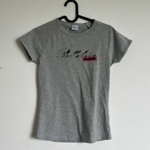 Grå t-shirt från Billabong - Säljer en grå t-shirt från Billabong med svart och röd logga framtill och tryck även på ryggen. T-shirten har rund hals och korta ärmar, perfekt för en avslappnad stil.
