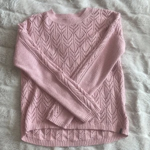 Ljusrosa stickad tröja med spetsmönster - Superfin ljusrosa stickad tröja med spetsmönster och rund halsringning. Tröjan har långa ärmar och ribbade muddar vid ärmslut och nederkant. Perfekt för lager-på-lager och ger en söt touch till din outfit.