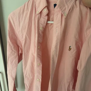 Ljusrosa skjorta från Ralph Lauren - Säljer en ljusrosa skjorta från Polo Ralph Lauren med klassisk button-down krage och broderad logga på bröstet. Slim fit-modell med långa ärmar och knappar framtill. Perfekt för dig som gillar stilrena plagg med snygg passform. Slim fit M men passar även S. 