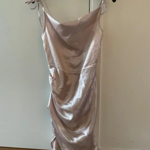 Champagnefärgad satin klänning - Lite insydd så var från början en S men passar S/XS elegant champagnefärgad klänning i satin med smala axelband och snygg drapering framtill. Klänningen har en figurnära passform och är perfekt för festliga tillfällen. Längden är mitt emellan kort och lång. 