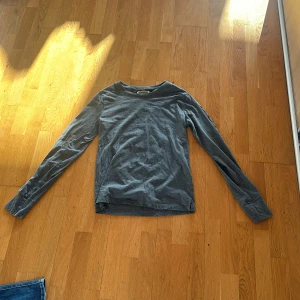 Grå långärmad tröja från Burberry - Säljer en stilren grå långärmad tröja från Burberry. Tröjan har en klassisk rund halsringning och är tillverkad i mjukt bomullsmaterial. Perfekt för en enkel och snygg look. Diskret Burberry-logga syns på etiketten.