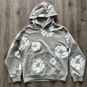 Grå denim tears hoodie - Grå hoodie med vita blommönster över hela tröjan. Mjuk och skön med huva och magficka. Perfekt för en avslappnad stil.