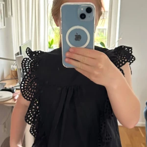 Svart blus med volang och broderade detaljer - Säljer en svart blus med volangmönstrade  ärmar och broderade håldetaljer. Mycket bra skick och är andvänd 5 ggr💕