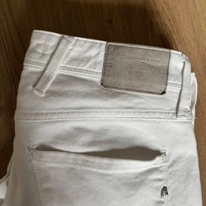 Vita Replay Anbass jeans - Säljer ett par vita Replay Anbass jeans med en klassisk design med silverfärgade knappar. Byxorna har en slim passform och är perfekta för dig som vill ha ett fräscht och stilrent par jeans till sommaren. Jeansen är använda ungefär 5 gånger. 