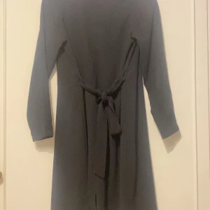 Svart kappa med knytband - Säljer en svart kappa med långa ärmar och knytband i midjan. Klänningen har en klassisk och stilren design som passar perfekt till många tillfällen. Enkel att styla med accessoarer för en personlig look.