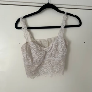 Vit spetsig croppad linnetopp - Säljer en vit croppad linnetopp med spetsdetaljer och smala axelband. Toppen har ett romantiskt och feminint utseende med vacker spets över hela ytan. Perfekt att styla till jeans eller kjol.