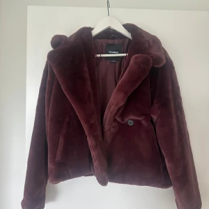 Vinröd pälsjacka från Pull&Bear - Säljer en vinröd pälsjacka från Pull&Bear. Jackan har en klassisk krage, stängs med knapp framtill och är helfodrad. Perfekt för dig som vill ha en mjuk och trendig jacka med lite lyxig känsla.