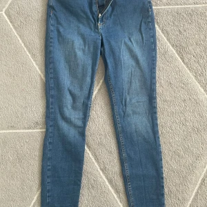 Blå skinny jeans med dragkedja - Säljer ett par klassiska blå skinny jeans med normalhög midja och dragkedja fram. Jeansen har fem fickor och bälteshällor, perfekta till vardags. Modellen är smal hela vägen ner och passar dig som gillar en tight passform.