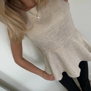 Glittrig peplumtop - Säljer denna skimriga beige-aktiga festtopp! Går att använda med vad som helst och sitter jättebra❤️