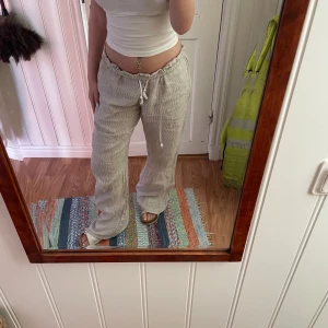 Beige linnebyxor från Brandy Melville - Säljer ett par beige linnebyxor från Brandy Melville med smala vita ränder och dragsko i midjan. Byxorna har använts max 3ggr, säljer då de är för långa.