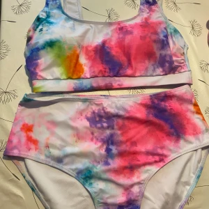 Färgglad bikini med tie-dye mönster - Säljer en superfin bikini med färgglatt tie-dye mönster i rosa, blått, lila, grönt och orange. Sportig topp med breda axelband och hög midja på underdelen. Perfekt för strand eller poolhäng!
