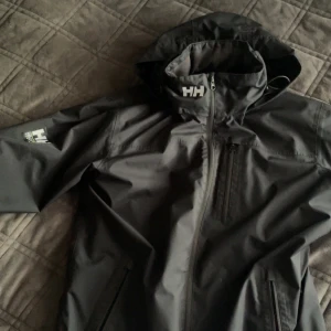 Svart vindjacka från Helly Hansen - Säljer en svart vindjacka från Helly Hansen med huva och dragkedja framtill.  kan tänka mig byta mot något också
