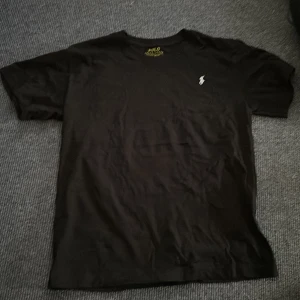 Svart t-shirt från Polo Ralph Lauren - Klassisk svart t-shirt från Polo Ralph Lauren med liten broderad logga på bröstet. T-shirten har rund hals och är kortärmad, perfekt för en stilren och enkel look. Tillverkad i mjuk bomull.
