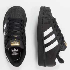 Adidas Superstar svartvita sneakers - Klassiska Adidas Superstar sneakers i svart med vita ränder och gulddetaljer på plösen. Skorna har snörning, rund tå och platt sula. Knappt använda, som nya. Storlek 38! 