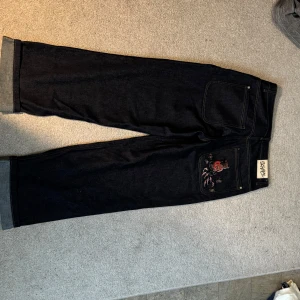 Mörkblåa jeans byxor med broderad detalj - Säljer ett par mörkblåa jeansbyxor från derschutze med breda ben och uppvikta benslut. 