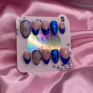 LunaGlow (S);Short Almond - Snygga handgjorda press-on naglar i storlek S med en mix av cateye/glitter/holografisk blå och nude bas. Två naglar har 3D blomma och små pärl/gulddetaljer. Perfekt för dig som vill ha en unik och färgstark look. Kommer i storlek S: 15 mm, 11,5 mm, 12 mm, 11 mm, 9 mm 