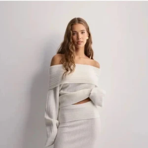 Offshoulder ribbad tröja i vitt - Säljer en vit offshoulder tröja med ribbad struktur. Tröjan har långa ärmar och en bred, vikt krage som ger en snygg och trendig look. Perfekt att styla med både kjol och jeans.
