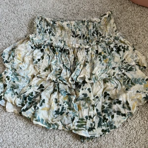 Blommig volangkjol med smock - Supersöt kort kjol med blommigt mönster i grönt och gult på ljus botten. Kjolen har bred smock i midjan och flera volanger 💚