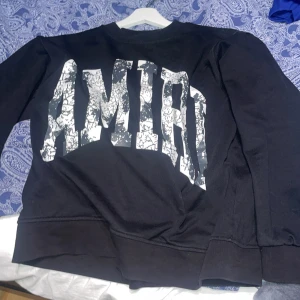 Svart sweatshirt från Amiri - Cool svart sweatshirt från Amiri med stort vitt tryck på ryggen. Tröjan har rund hals och långa ärmar, perfekt för en avslappnad streetwear-look.  äkta men använt mycket 