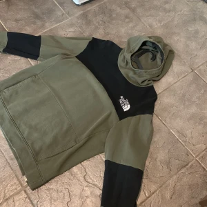 The North Face hoodie  - Säljer en snygg hoodie från The North Face i olivgrönt och svart. Tröjan har en stor magficka, huva och logga på bröstet. Perfekt för chill dagar eller när du vill ha en streetwear-look. Bra skick men använd