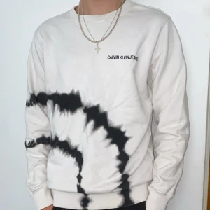 Vit och svart tie-dye sweatshirt från Calvin Klein Jeans - Orginalpris runt 1499 och aldrig använt denna. Säljer en vit sweatshirt från Calvin Klein Jeans med svart tie-dye mönster runt hela tröjan. Tröjan har rund halsringning och långa ärmar. Loggan är broderad på bröstet. Perfekt för en avslappnad och trendig stil. 